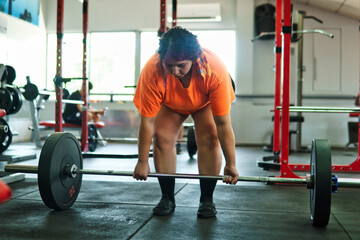 View of a beautiful, overweight young Latina lifting weights and working out at a gym. Positively, she's pushing herself to the limit. She's improving and feeling better.