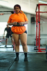 Beautiful young overweight Latina breathing and tired after lifting weights at the gym. Wearing colorful clothes, hair, and retro makeup. Positive, pushing herself to the limit. Improvement and well-b