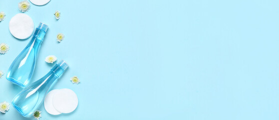 Bottles of micellar water, cotton pads and flowers on blue background