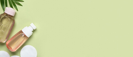 Bottles of micellar water, cotton pads and leaves on green background