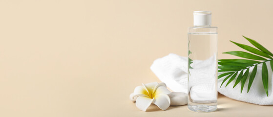 Bottle of micellar water, towel, flower and green leaf on beige background, closeup