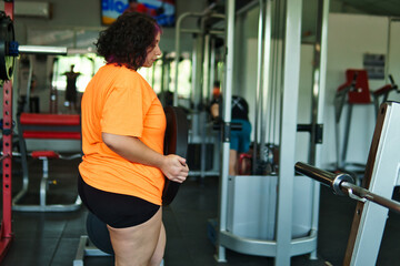 View of an overweight young Latina woman carrying weights and preparing to workout at a gym. Pushing herself. Improvement and well-being.