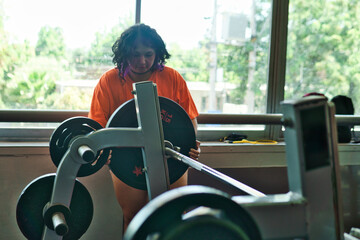 View of an overweight young Latina woman carrying weights and preparing to workout at a gym. Pushing herself. Improvement and well-being.