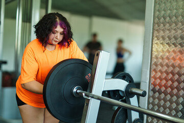 View of an overweight young Latina woman carrying weights and preparing to workout at a gym. Pushing herself. Improvement and well-being.