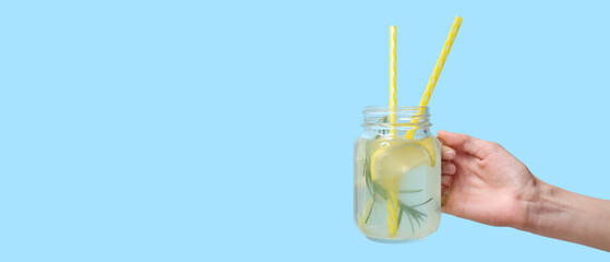 Female hand with mason jar of fresh lemonade on color background