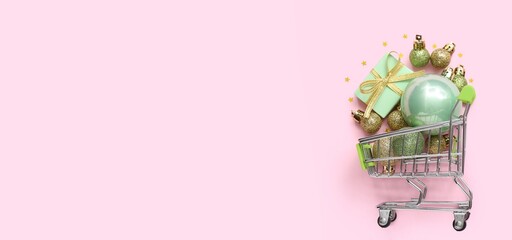 Small shopping cart, Christmas balls and gift on pink background with space for text
