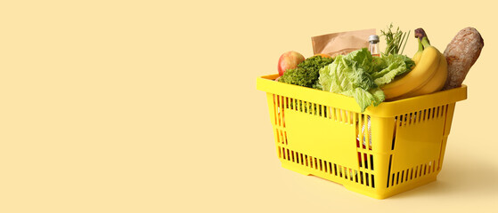 Yellow shopping basket full of different fresh products and apples on beige background