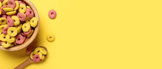 Bowl and spoon with corn cereal rings on yellow background with space for text