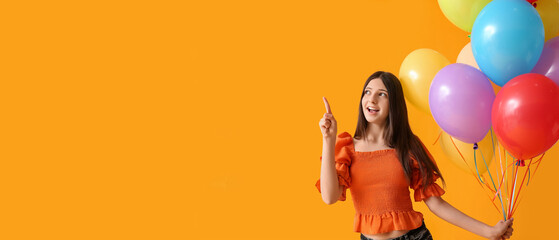 Teenage girl with colorful balloons pointing at something on orange background with space for text