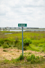 A street sign in the grass with water and a bridge in the background. 