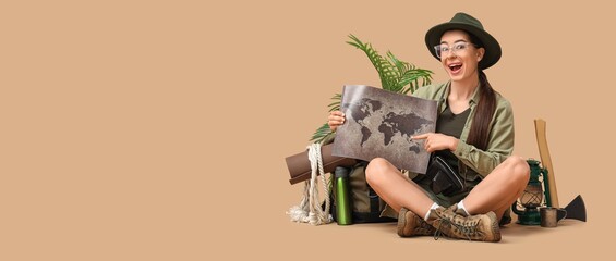 Excited female tourist with map and traveling equipment sitting on beige background with space for...