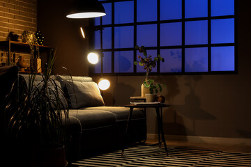 Interior of dark living room with cozy sofa, coffee table and glowing lamps