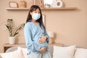Pregnant Asian woman in medical mask at home