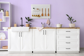 Interior of stylish kitchen with utensils on pegboard, sink and white counters