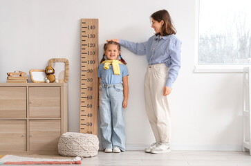 Mother measuring her little daughter's height near stadiometer at home