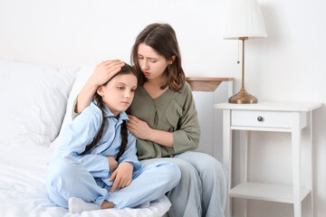 Cute girl suffering from bellyache with her mother in bedroom