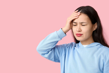 Young Asian woman suffering from headache on pink background. Brain Injury Awareness Month
