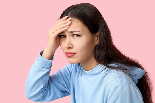 Young Asian woman suffering from headache on pink background. Brain Injury Awareness Month