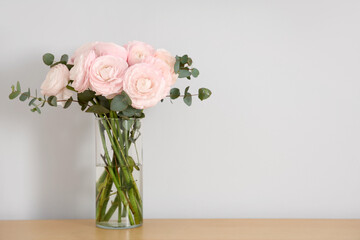 Vase with bouquet of beautiful ranunculus flowers on table near beige wall, closeup