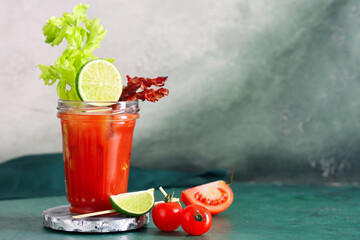 Glass of bloody mary cocktail with bacon, lime and celery on green table