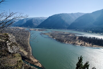 Aerial View of Columbia River, surrounded by massive pine trees, and huge rock cliffs under a clear blue sky.