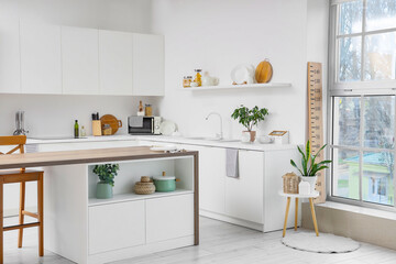 Interior of modern kitchen with wooden stadiometer, houseplants, microwave and kitchenware on counter