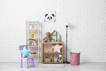 Obraz premium Interior of children's room with many toys in shelving units, chair and lamp near white brick wall
