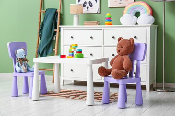 Interior of children's room with lamp, ladder, play table and many toys on commode near green wall