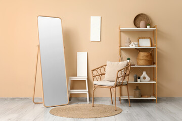 Interior of living room with armchair, mirror and home decor in shelving unit near beige wall