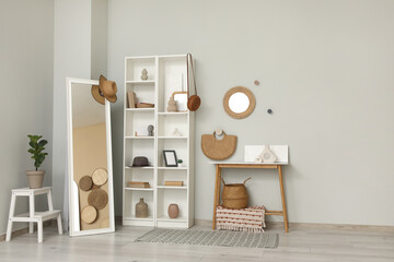 Obraz premium Interior of living room with shelving unit, mirrors and home decor on table near grey wall