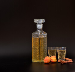 Apricot liqueur with anise and cinnamon in a crystal decanter and two glasses on a black background.