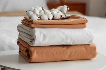 Stack of clean bed sheets with cotton flowers sprig on table in bedroom