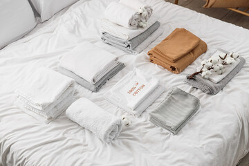 Stacks of clean bed sheets with towels, cotton flowers and paper in bedroom, top view