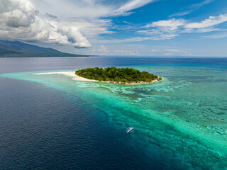 Mantigue Island with white sand beach under blue skies and clouds. Turquoise water atoll and coral reefs. Camiguin, Philippines.