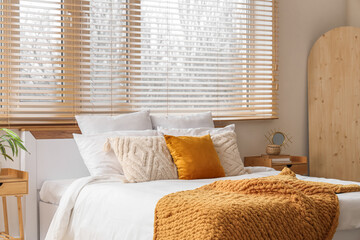 Interior of bedroom with big bed, bedside tables, wooden board and stylish wooden blinds on window