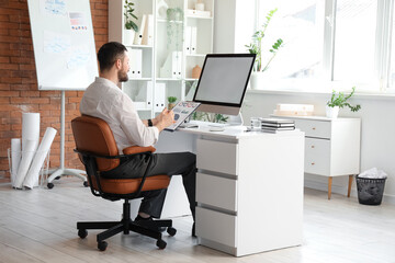 Young businessman working with clipboard and blank computer at table in office