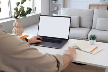 Young man working with blank laptop at table in office, closeup