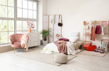 Interior of messy children's room with bed, clothes rack and folding screen