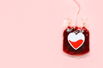 Blood pack for transfusion with paper heart on pink background. Blood donation concept