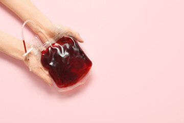 Female hands with blood pack on pink background. Blood donation concept