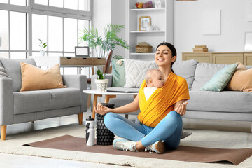 Sporty mother with her baby in sling meditating at home