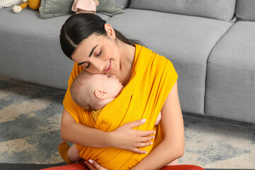 Sporty young woman with her baby in sling at home