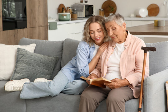 Senior woman with her granddaughter reading book on sofa at home