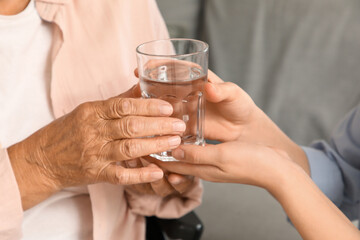 Senior woman taking glass of water from her granddaughter at home, closeup