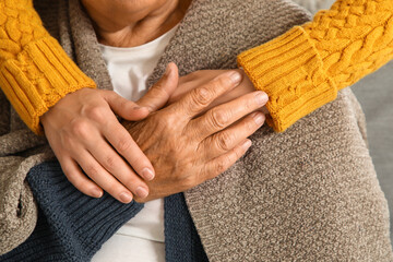 Young caregiver hugging senior woman with plaid at home, closeup