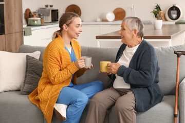 Young caregiver with senior woman drinking tea in kitchen