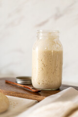 Freshly prepared sourdough bread dough rests on parchment near a container of active starter and a mixing bowl, showcasing the art of home baking.