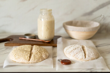 Freshly prepared sourdough bread dough rests on parchment near a container of active starter and a mixing bowl, showcasing the art of home baking.