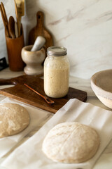 Freshly prepared sourdough bread dough rests on parchment near a container of active starter and a...