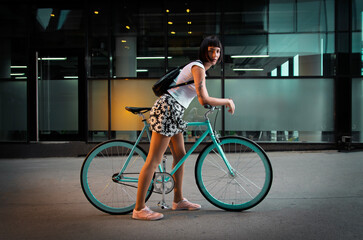 Beautiful Urban hipster tattooed girl with short black hair posing on the bicycle in the city 